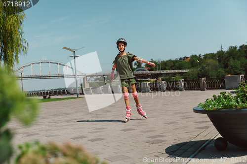 Image of Teenage girl in a helmet learns to ride on roller skates outdoors