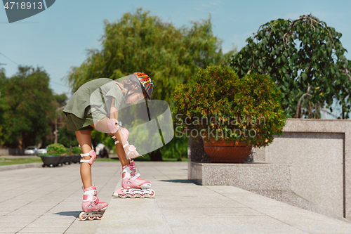 Image of Teenage girl in a helmet learns to ride on roller skates outdoors