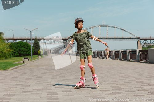 Image of Teenage girl in a helmet learns to ride on roller skates outdoors