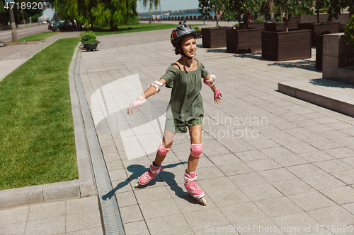 Image of Teenage girl in a helmet learns to ride on roller skates outdoors