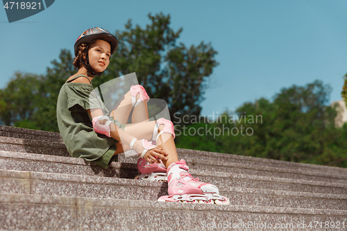 Image of Teenage girl in a helmet learns to ride on roller skates outdoors