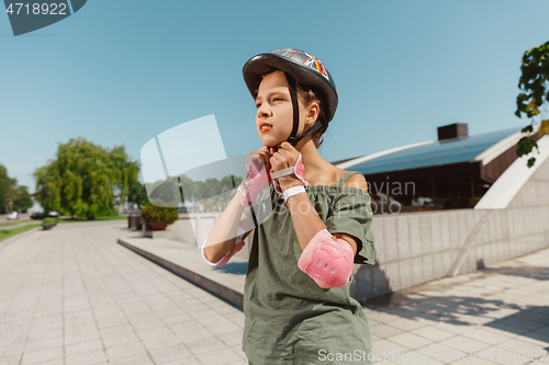 Image of Teenage girl in a helmet learns to ride on roller skates outdoors