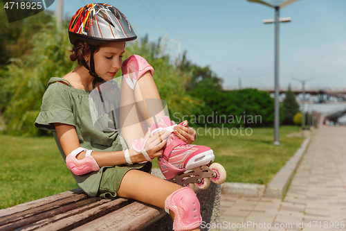 Image of Teenage girl in a helmet learns to ride on roller skates outdoors