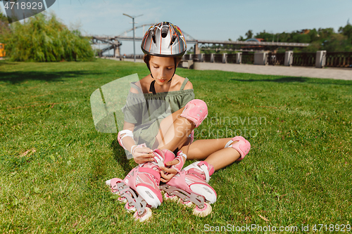 Image of Teenage girl in a helmet learns to ride on roller skates outdoors