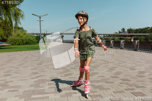 Image of Teenage girl in a helmet learns to ride on roller skates outdoors
