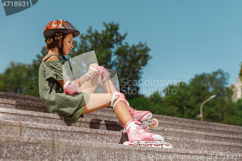 Image of Teenage girl in a helmet learns to ride on roller skates outdoors