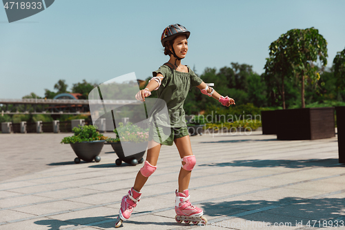 Image of Teenage girl in a helmet learns to ride on roller skates outdoors