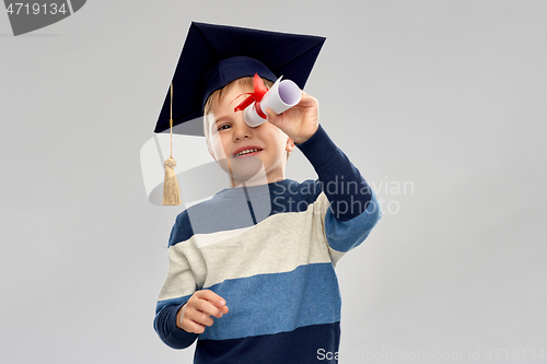 Image of little boy in mortarboard looking through diploma