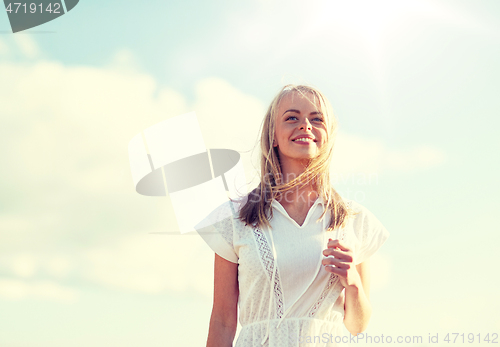 Image of smiling young woman in white dress over blue sky