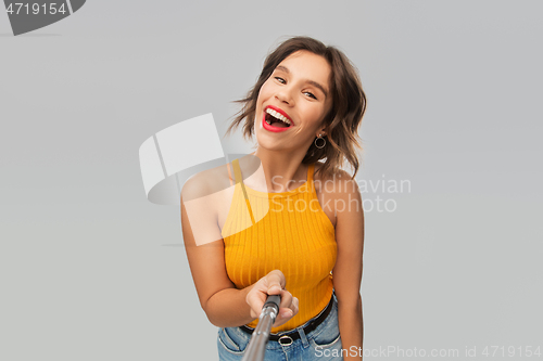 Image of happy young woman taking picture by selfie stick