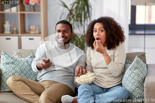 Image of african couple with popcorn watching tv at home