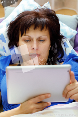 Image of Middle age woman resting in bed with tablet