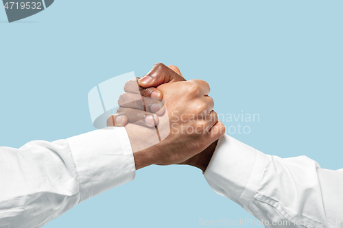 Image of Two male hands competion in arm wrestling isolated on blue studio background