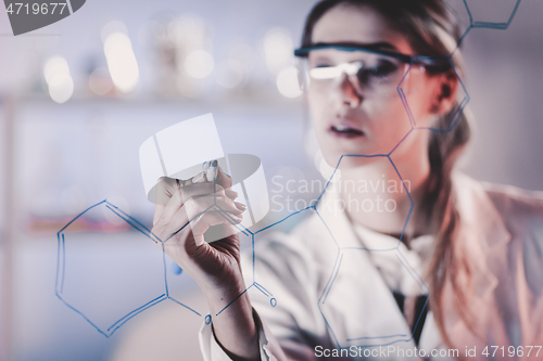 Image of Portrait of a confident female researcher in life science laboratory writing structural chemical formula on a glass board.