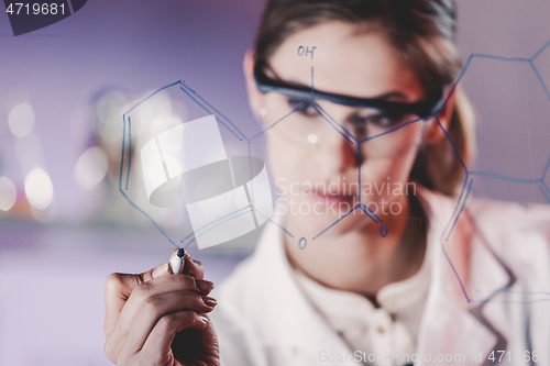 Image of Portrait of a confident female researcher in life science laboratory writing structural chemical formula on a glass board.