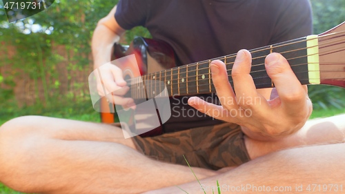 Image of Man sitting in the grass playing guitar