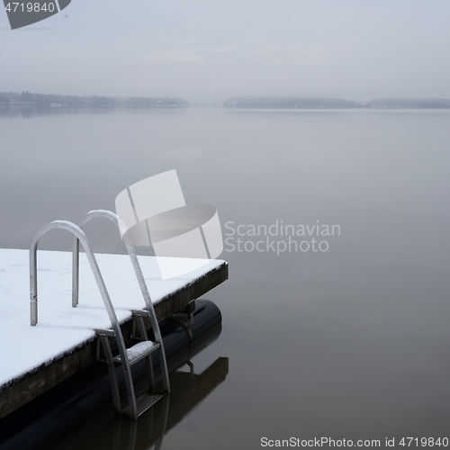 Image of wooden pier and ladder on the lake covered with snow