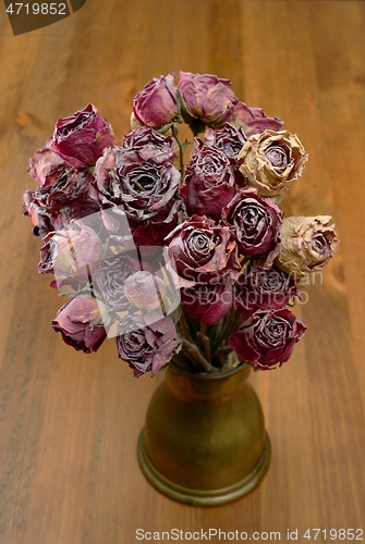 Image of a bouquet of dry roses in a copper coffee turk on a wooden backg