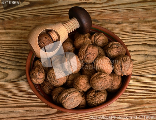 Image of walnuts in a bowl and a wooden nutcracker on a wooden backdrop