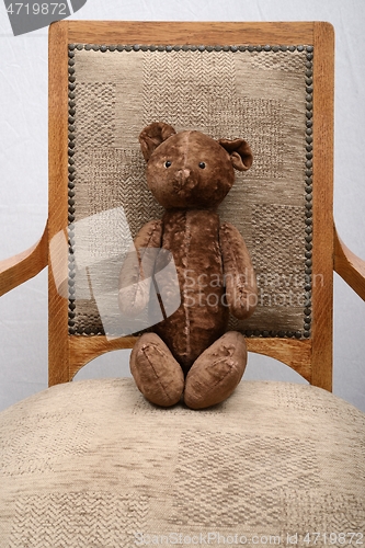 Image of shabby teddy bear sitting in an old vintage armchair