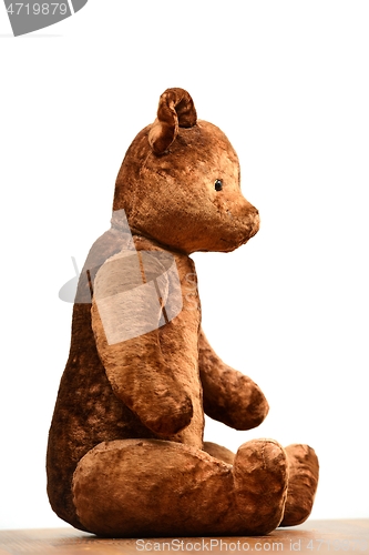 Image of shabby teddy bear toy sits sideways on a white 