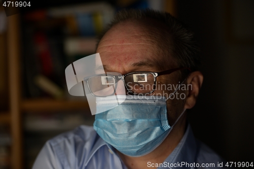Image of a man wearing glasses and a protective medical mask in front of 
