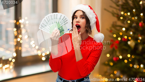 Image of surprised woman in santa hat with money