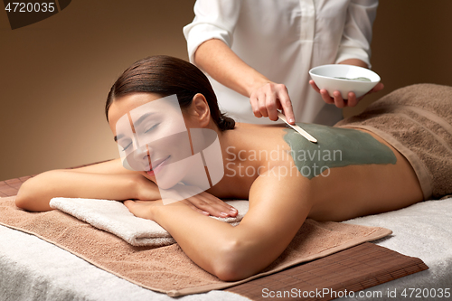 Image of woman and cosmetologist applying clay mask in spa