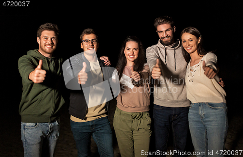 Image of happy smiling friends showing thumbs up at night