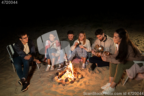 Image of friends roasting marshmallow on camp fire on beach