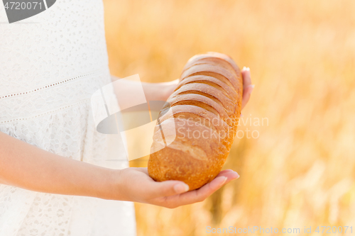 Image of hands holding loaf of white bread on cereal field