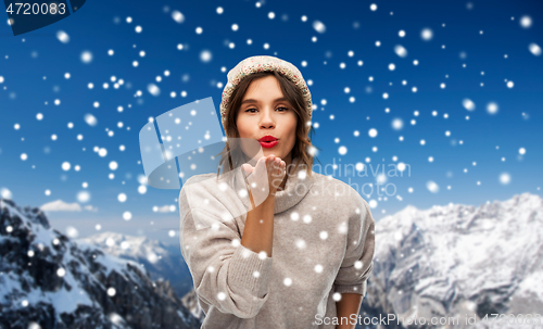 Image of young woman in knitted winter hat sending air kiss