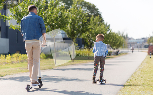 Image of happy father and little son riding scooter in city