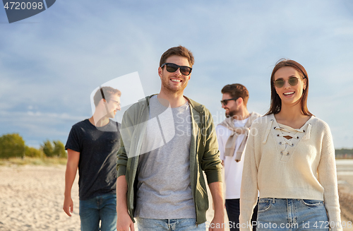 Image of happy friends walking along summer beach