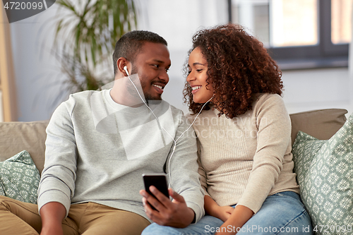 Image of happy couple with smartphone and earphones at home