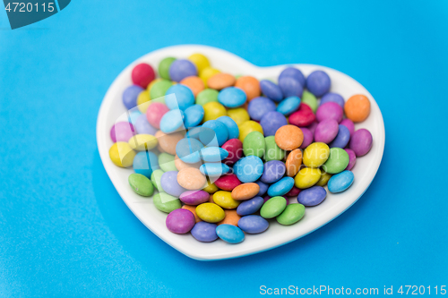 Image of candies on heart shaped plate over blue background