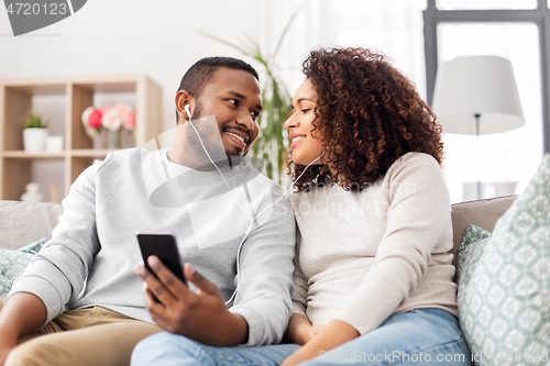 Image of happy couple with smartphone and earphones at home