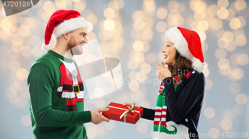 Image of happy couple in christmas sweaters with gift box