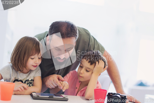 Image of single father at home with two kids playing games on tablet