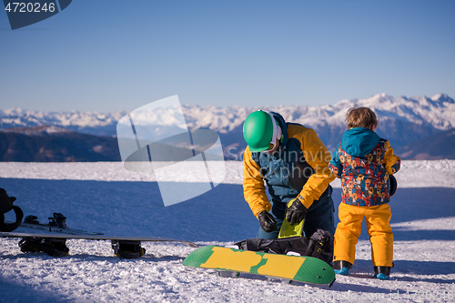 Image of father preparing his little son for the first time on a snowboar