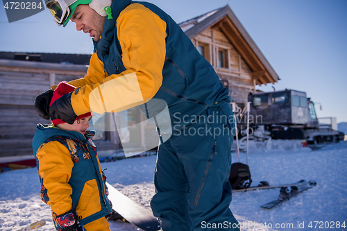 Image of father preparing his little son for the first time on a snowboar