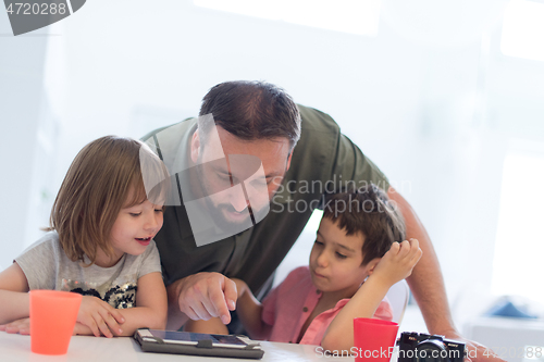 Image of single father at home with two kids playing games on tablet