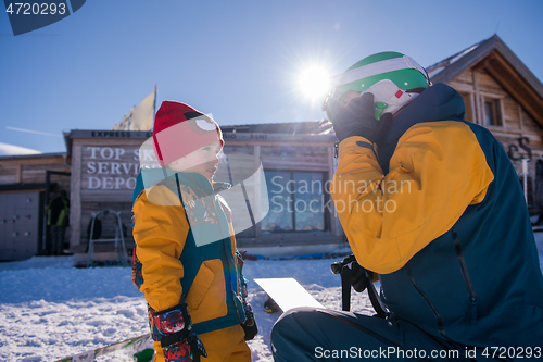 Image of father preparing his little son for the first time on a snowboar