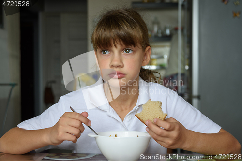 Image of Girl thoughtfully eats soup at the table in the kitchen