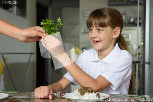 Image of The girl happily takes fresh herbs from her mother\'s hands at lunch