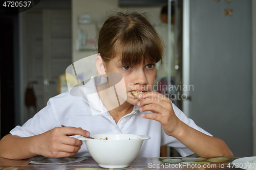 Image of Tired hungry schoolgirl eating soup at the table in the kitchen