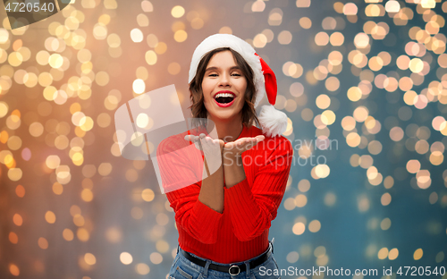 Image of happy young woman in santa hat sending air kiss