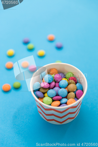 Image of candy drops in paper cup on blue background