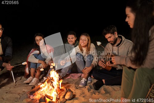 Image of friends roasting marshmallow on camp fire on beach