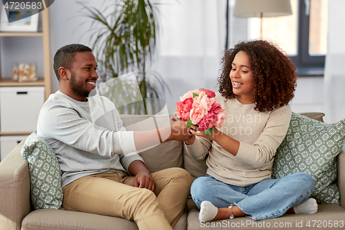 Image of happy couple with bunch of flowers at home